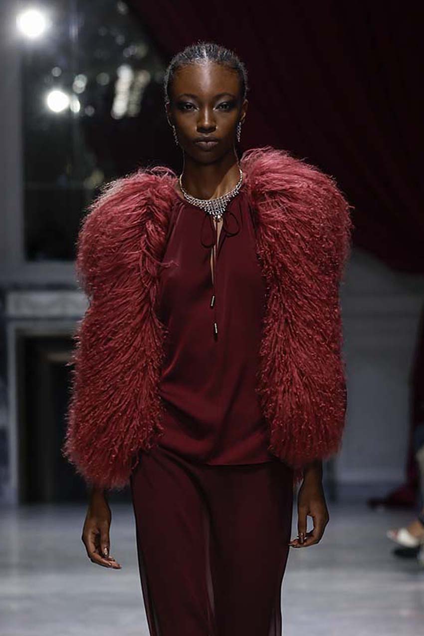 Model wearing a red fluffy coat and matching outfit on a runway.