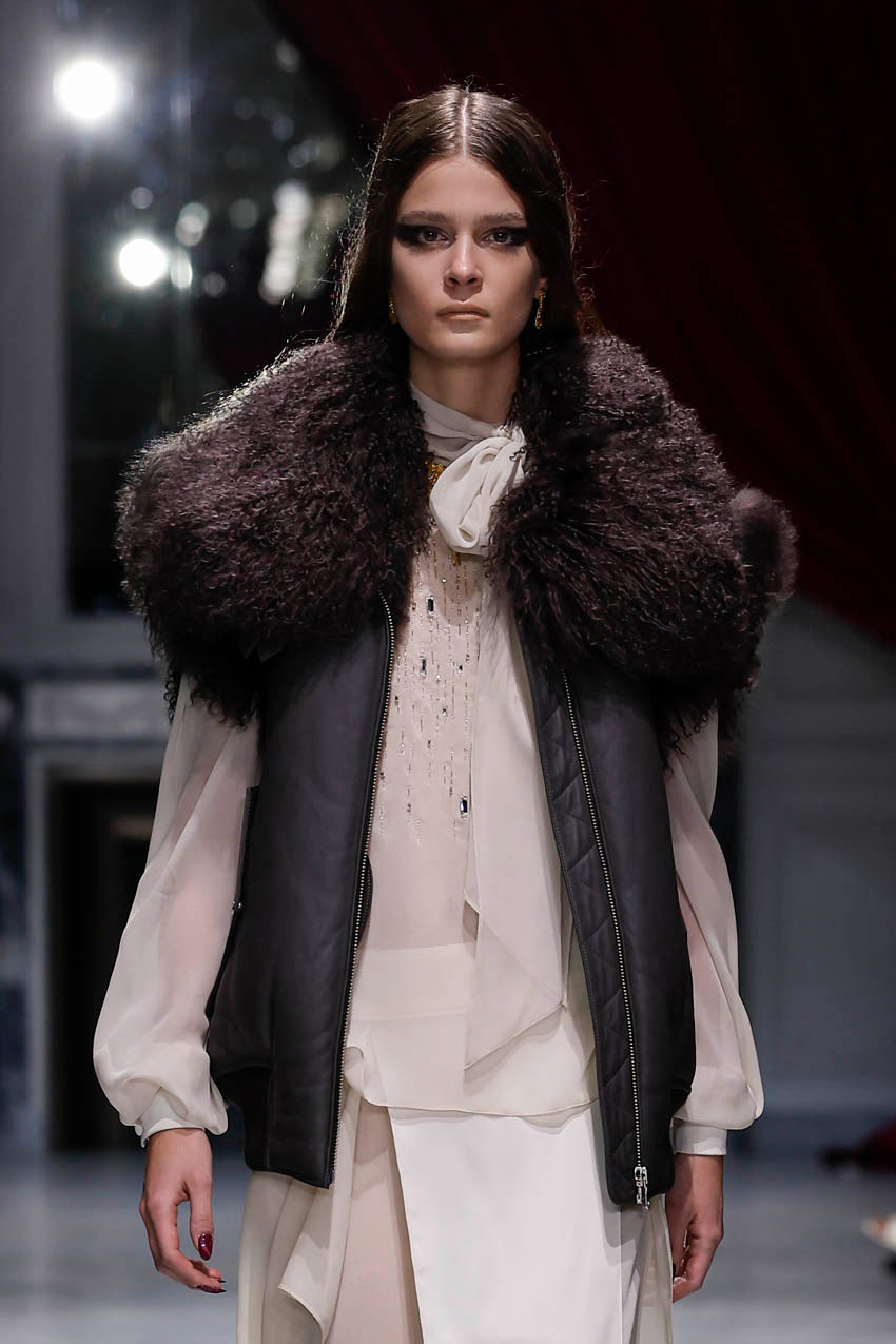Model wearing a fur vest and layered outfit on a runway