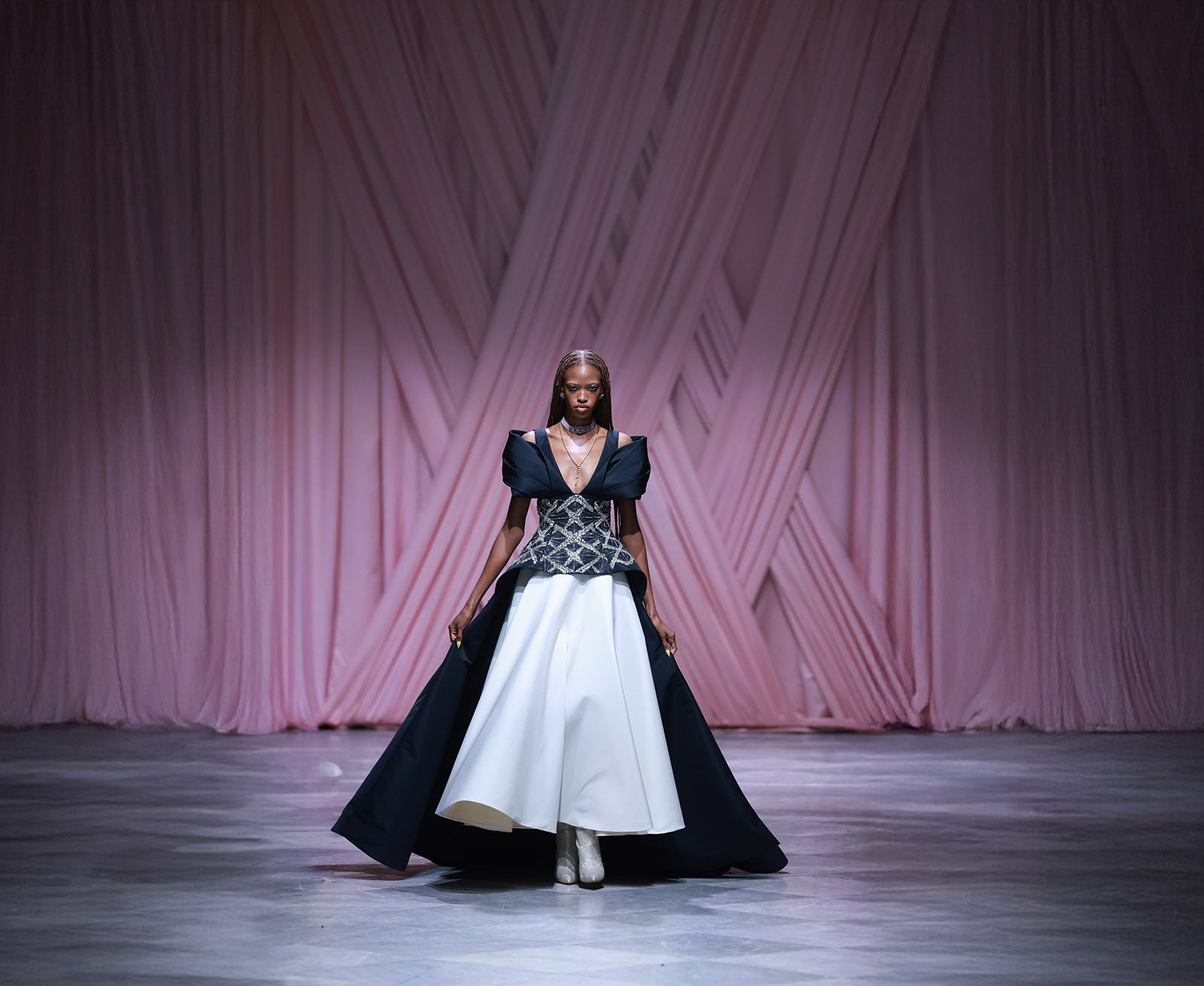 Model wearing a black and white dress on a runway with a pink textured backdrop