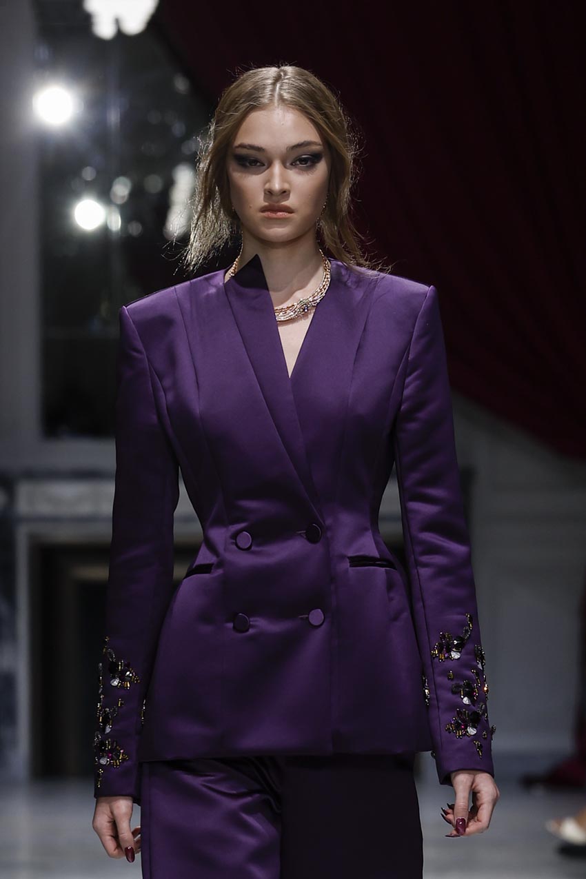 Model wearing a purple suit with embellishments on a runway.