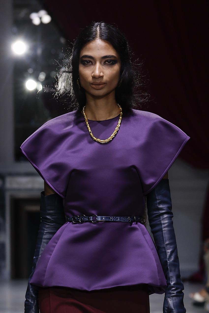 Model wearing a purple outfit with leather gloves on a runway.