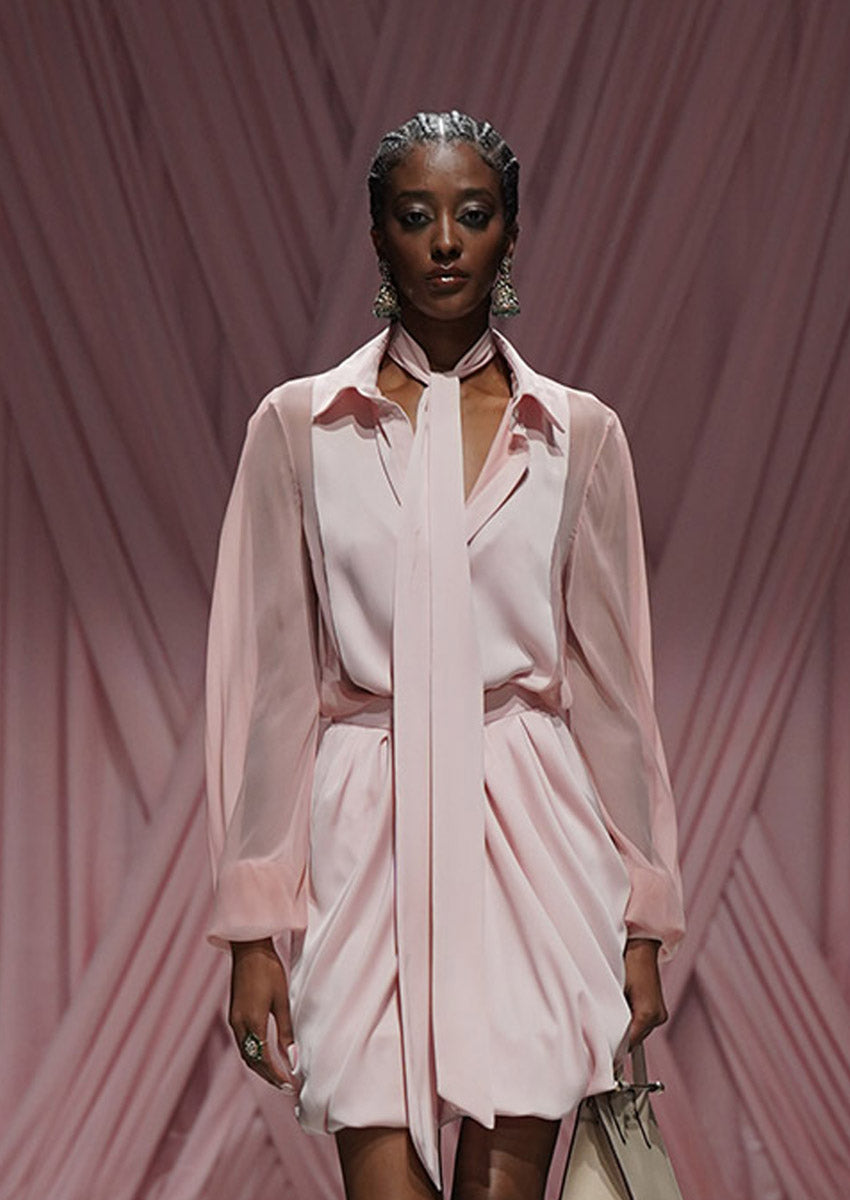 Woman wearing a light pink outfit against a pink draped curtain background